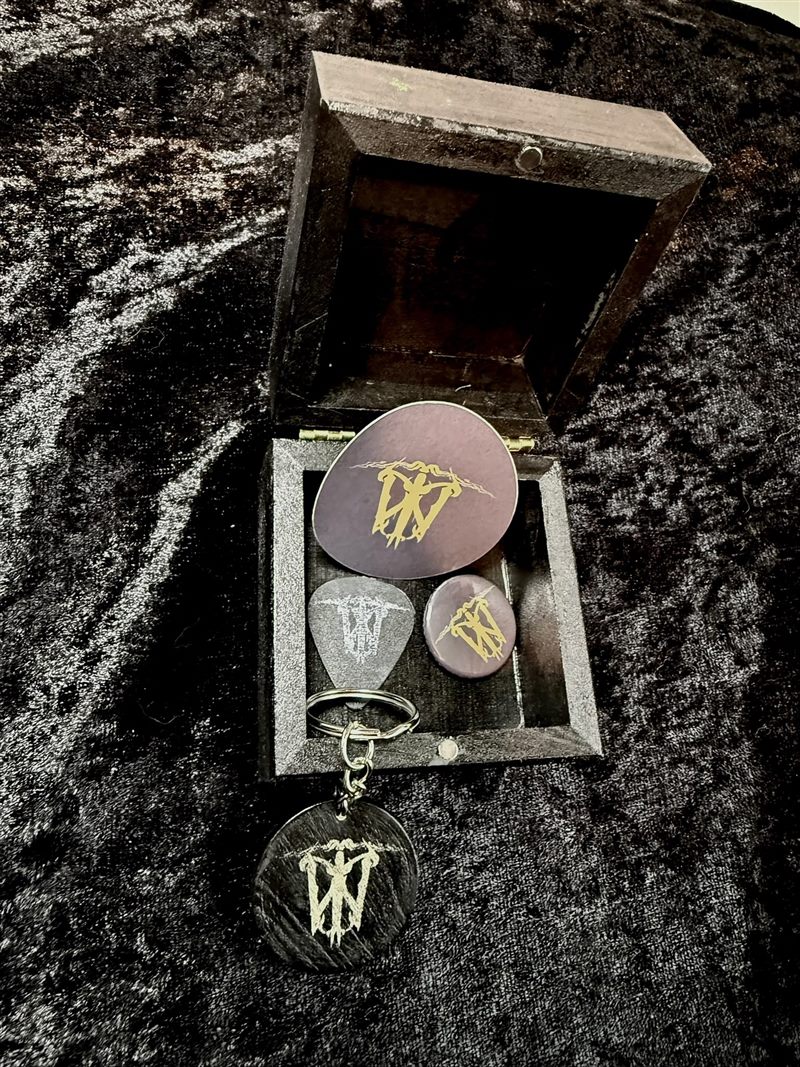 Open black wooden bundle box showing the sigil sticker, guitar pick, pin badge and keyring